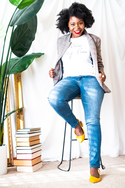 woman wearing stylish jeans, t- shirt and blazer sitting on a bar stool to a tall plant