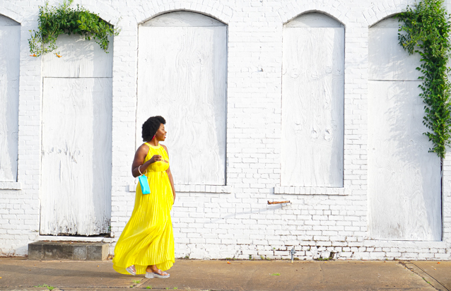 Yellow Pleated Dress styled for Summer by top Atlanta fashion blogger, Hurry in Time: Woman wearing a yellow dress waling with her shades in her hands. 