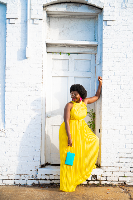 Yellow Pleated Dress styled for Summer by top Atlanta fashion blogger, Hurry in Time: Woman wearing a yellow dress with her elbow on the wall posing. 